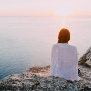 Femme assise sur un rocher face à la mer